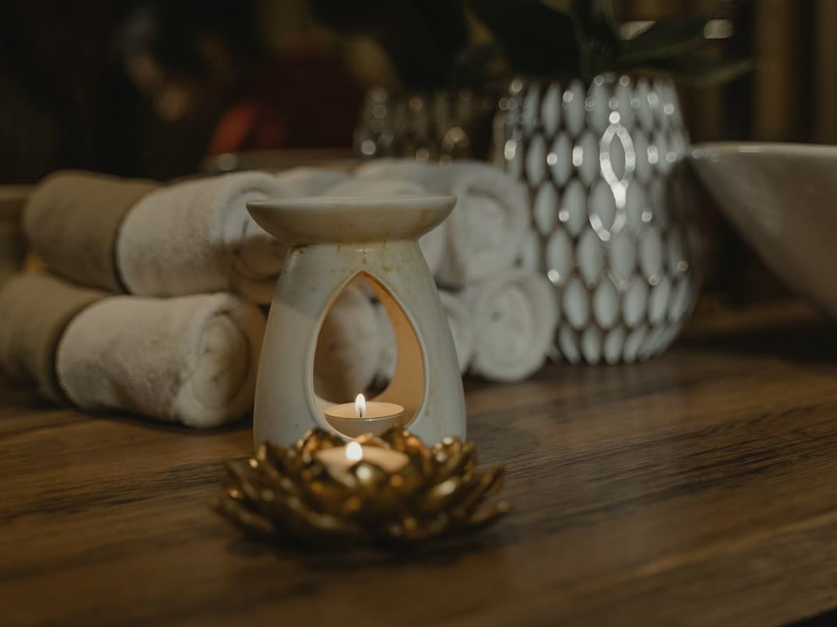 Lit candle in a calm, warm spa setting with rolled towels