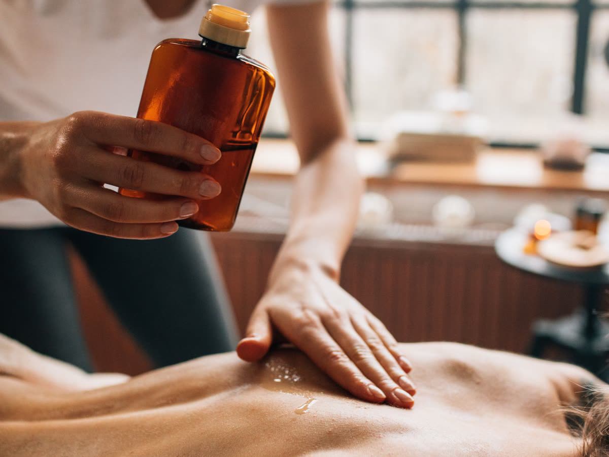 Amber bottle of massage oil being poured during a back massage